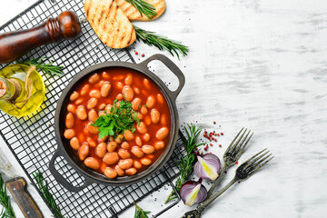 Boiled beans in tomato sauce with parsley and spices in a black metal pan. Rustic style. Top view.