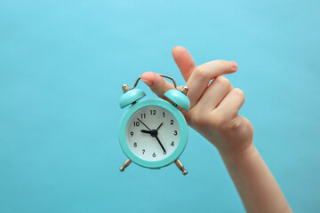 A child holds a small blue alarm clock on a blue background.