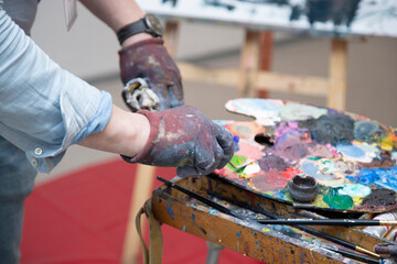 The artist paints with a brush on canvas with colored oil paints