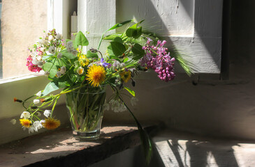 Glass vase with a bouquet of wildflowers standing on a vintage tuscan window sill 