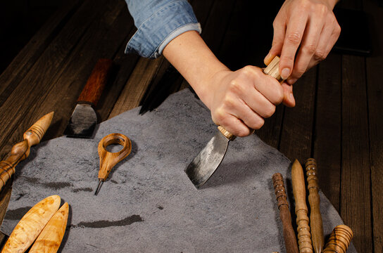 Tilt down of female shoemaker circling stencil lying on piece of brown leather using special pen
