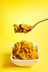 fork picking up some yellow rice with vegetables from a bowl. Food concept