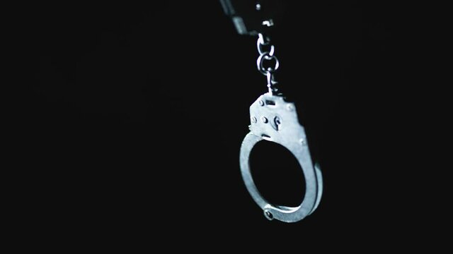 The police is giving the handcuff to a prisoner. Detention of a suspect. Red and blue light from a police flashers.