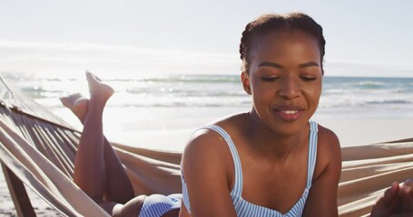 African american woman using digital tablet while lying on a hammock at the beach