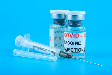 Covid-19 coronavirus vaccine concept - two glass vials with metal caps on blue background with injection syringe. Vaccination against 2019-nCoV virus.