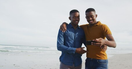African american twin brothers standing on a beach using a smartphone - Powered by Adobe