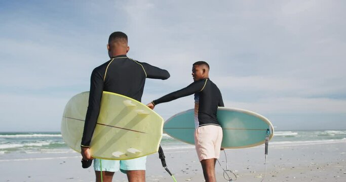 African american teenage twin brothers walking on a beach carrying surfboards
