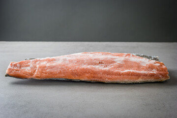 Frozen salmon fillet with skin on a grey background