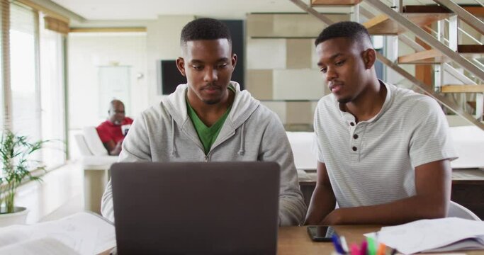Two african american teenage twin brothers using a laptop and talking with father in background