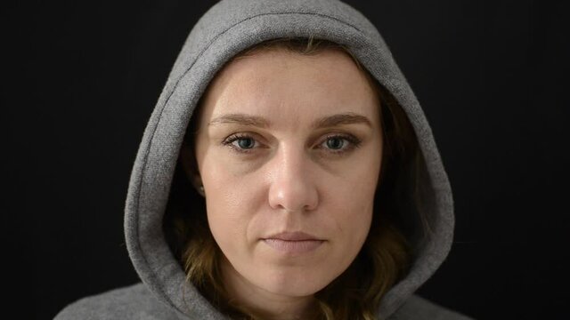 Young woman in sports jacket with hood, taking off medical protective mask from face, isolated on black background