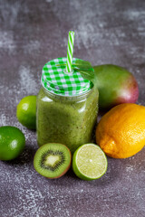 Healthy fresh fruit smoothie drink surrounded by kiwi lime and lemon on gray