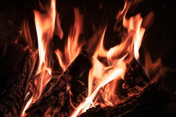 Fiery yellow orange tongues on dark background rise up in a brick fireplace burning flame, toned in...