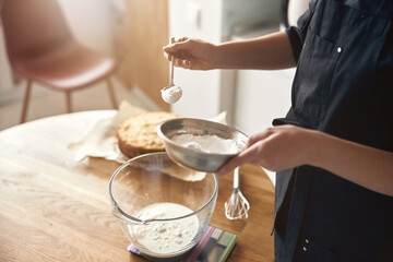 young professional female cook is preparing tasty cake at her light modern kitchen