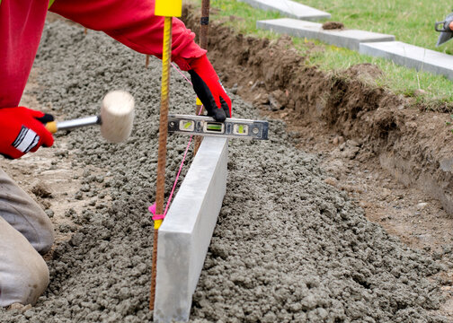 Laing edging kerb on semidry concrete during roadworks and new footpath construction by groundworker wearing safety gloves