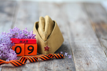 Wooden calendar with Russian text May 9, garrison cap, george ribbon and a bouquet of lilacs on a...