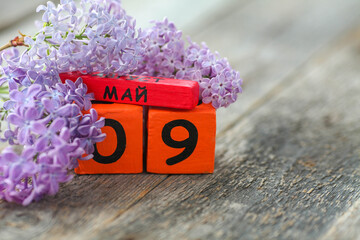 Wooden calendar with Russian text May 9 and a bouquet of lilacs on a wooden background. Victory...