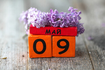 Wooden calendar with Russian text May 9 and a bouquet of lilacs on a wooden background. Victory...