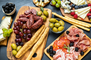 Charcuterie board with pork sausage, salami and cheese plate with brie, parmesan pecorino and gorgonzola. served with grapes. olives and blueberries with grissini breadsticks. food flat lay