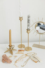 Modern gold jewellery, hair clips on white table with vintage candles and boho mirror. Accessories