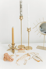 Modern gold jewellery, hair clips on white table with vintage candles and boho mirror. Accessories