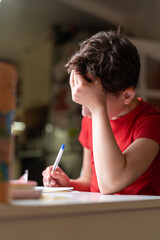 Attentive schoolboy boy sits at the table and does his homework, looks at the textbook, at home. Back to school. The child is tired of studying. End of the school year.