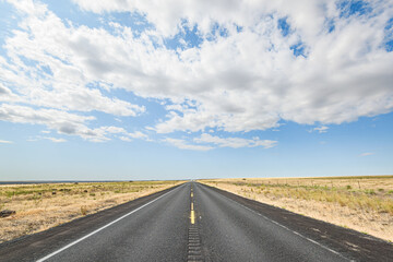 Ribbon of blacktop disappears into the distance in the center of the frame in the American West