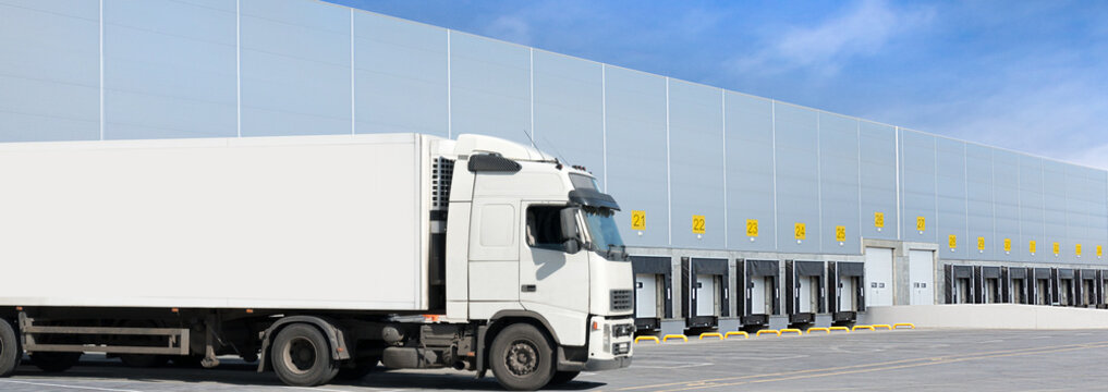 Loading docks of large warehouse with white truck under loading