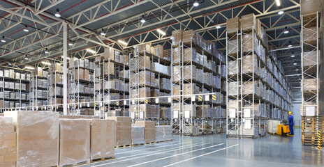 Huge distribution warehouse with high shelves and forklift with young driver.