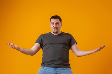 An angry inadequate violent emotionally unstable person with a dissatisfied expression gestures with his hands on a yellow background in the studio. Aggressive behavior