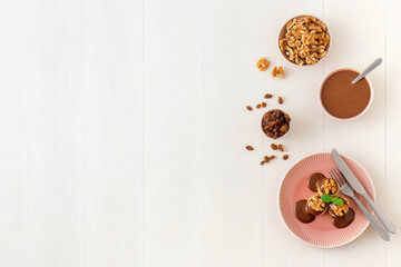 Pancakes stuffed with raisins and crushed walnuts, with chocolate cream topping. Top down view. White wooden table. No people.