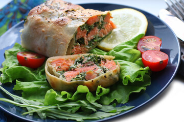 Strudel with salmon, spinach, cheese, arugula, lemon and tomatoes on blue plate 