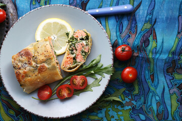 Strudel with salmon, spinach, cheese, arugula, lemon and tomatoes on blue background. Top view
