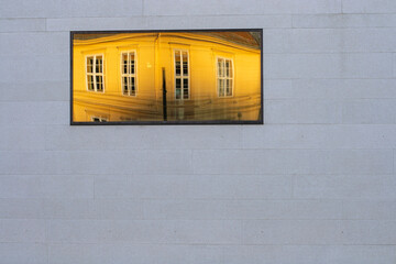 Yellow building reflecting on the window of a grey wall. Concrete wall with big window. 