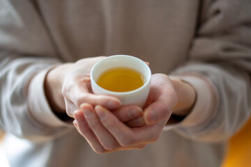 woman holding a small warm cup of tea in her hands. No face, blurred background.