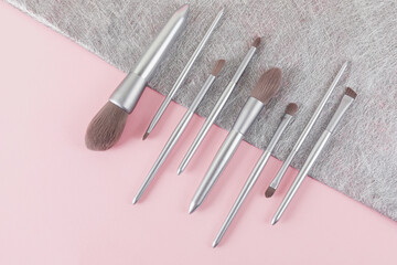 Set of silver color professional makeup brushes in isometric line on pink and gray colored composed background. Creative concept of beauty. Copy space. Flat lay.