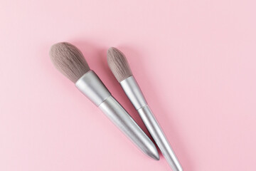 Two silver color professional makeup brushes on pink colored background. Creative concept of beauty. Copy space. Flat lay.