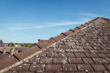 A triangle or hip roof end showing the ridge with capped angle tiles, mortar and lichen on the old traditional stone slates