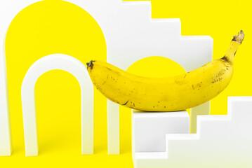 Aesthetic minimalism food photography. Banana on yellow background. Abstract scene with white geometrical forms. 