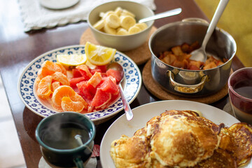Brunch pancakes with citrus fruits, homemade apple jam, bananas and steaming, hot cup tea or coffee. 