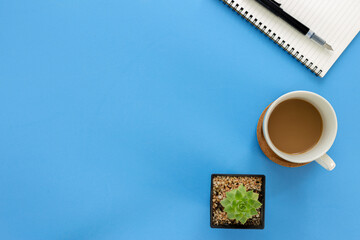 Top view notebook with coffee cup and cactus isolated on blue background with copy space