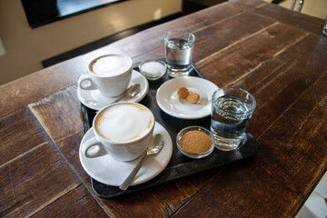 coffee in the morning, two cups of latte on wood table in cafe or coffeeshop with sugar, a glass of water and amaretti cookie