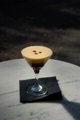Coffee cocktail with foam and coffee beans on the top standing on a marble table. Dark background