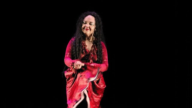 A beautiful gypsy woman with long hair in a red suit dances incendiaryly on a black background