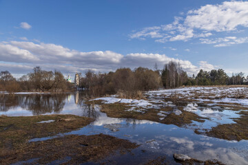 River flood on a spring day. Dry grass is visible from under the snow. The land is flooded with water.