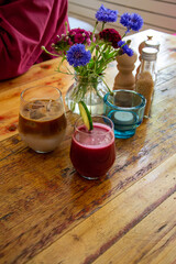 Ice refreshing sweet coffee and beetroot smoothie, juice with cucumber on a rustic table in cafe next to spring flowers.