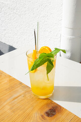 Glass with lemonade or mojito cocktail with orange and mint, cold refreshing drink or beverage with ice on wood and white background. 