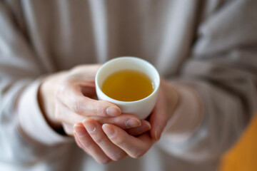 woman holding a small cup of tea with hands. Green tea.  Blurred background selective focus.