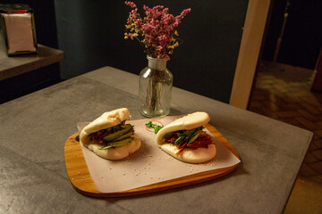 Asian burger, sandwich with pulled pork. Steamed bun burger on cutting board with flowers. Gua bao.