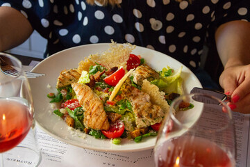 grilled chicken and vegetable salad with fried cheese eaten by a woman with red wine