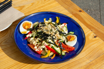 Asian fusion vegetable noodle dish with seaweed and eggs on a blue dish. 